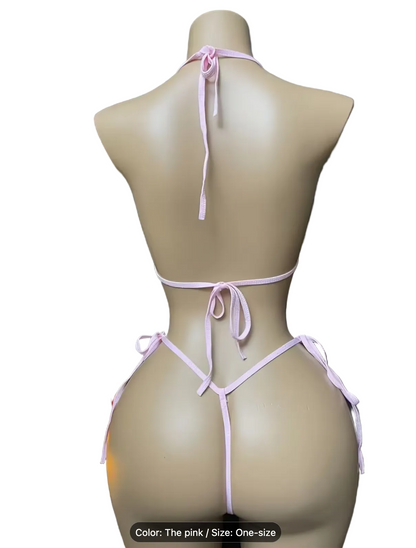 A mannequin torso shown from the back wearing a light pink string bikini bottom and matching halter-style top. A Christmas tree and lit candles sit to the left against a dark background, with text at the bottom reading 'Color: The pink / Size: One-size'.